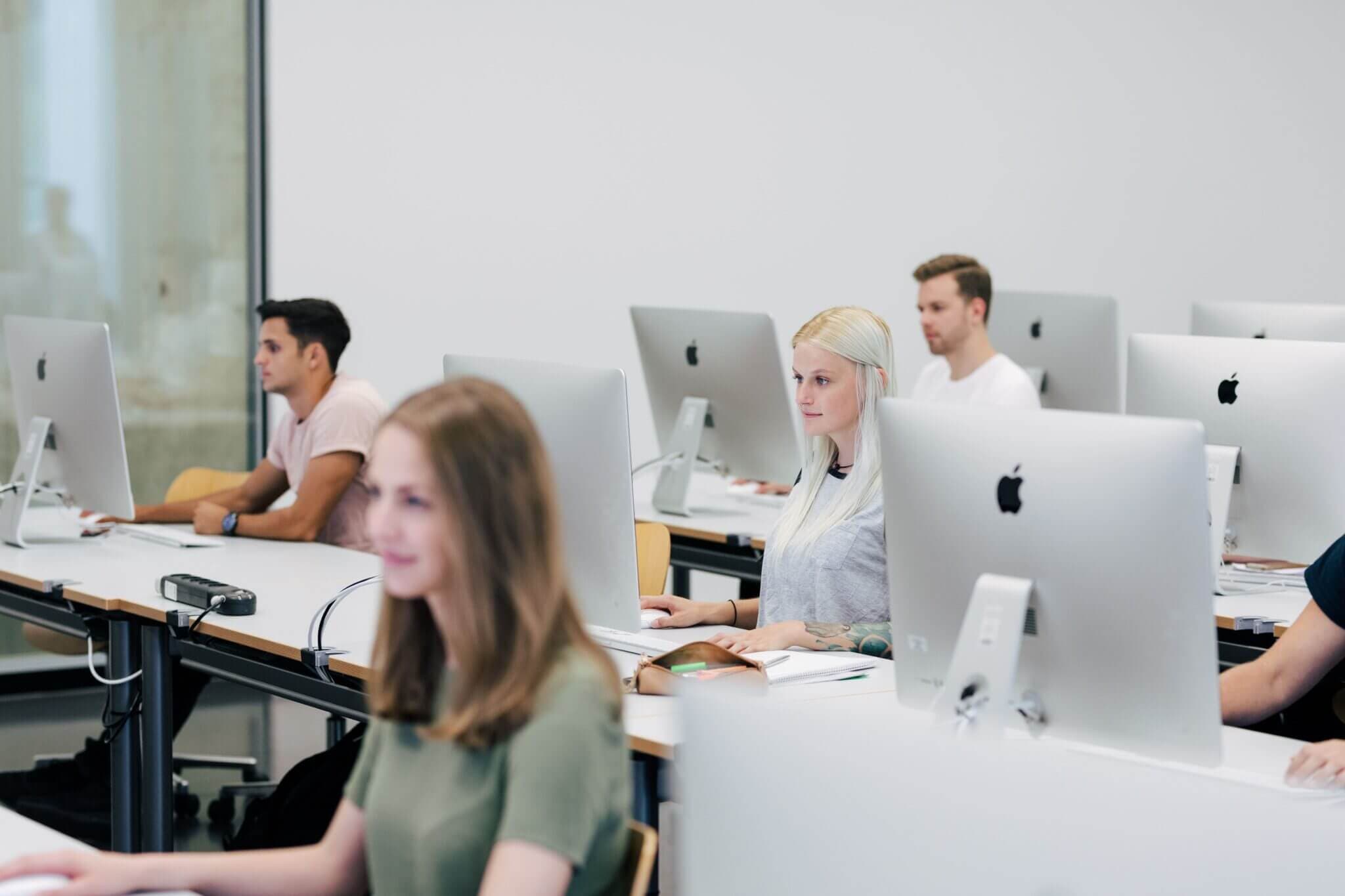 Menschen sitzen in einem Kursraum und arbeiten konzentriert am Computer.